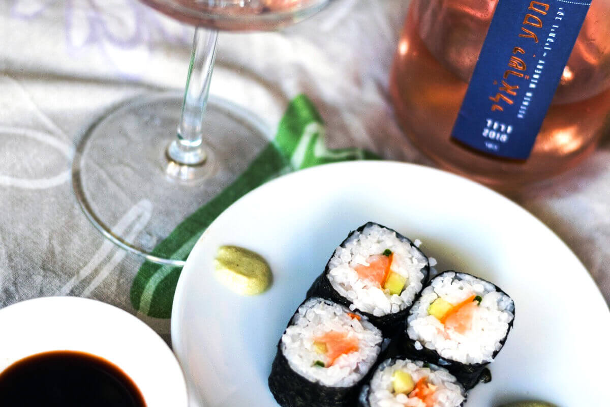 Makirullar med lax och gurka på en tallrik med ett glas rosé